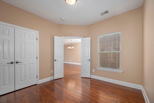 unfurnished bedroom with dark hardwood / wood-style floors, a closet, and a notable chandelier