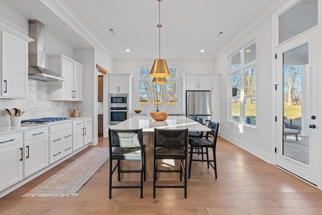 kitchen with appliances with stainless steel finishes, white cabinetry, hanging light fixtures, decorative backsplash, and wall chimney exhaust hood