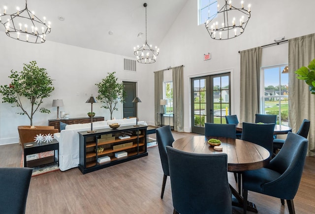 dining area with french doors, wood-type flooring, a notable chandelier, and a towering ceiling