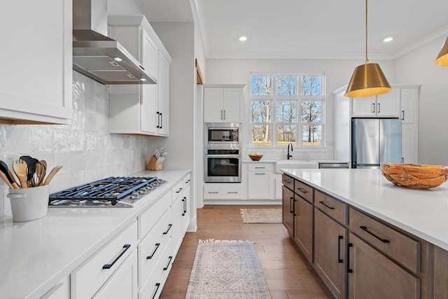 kitchen featuring white cabinets, pendant lighting, appliances with stainless steel finishes, and wall chimney exhaust hood