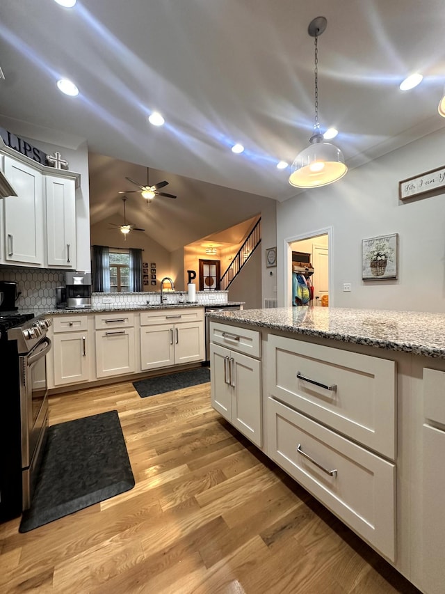 kitchen featuring light stone countertops, white cabinets, lofted ceiling, gas stove, and decorative backsplash