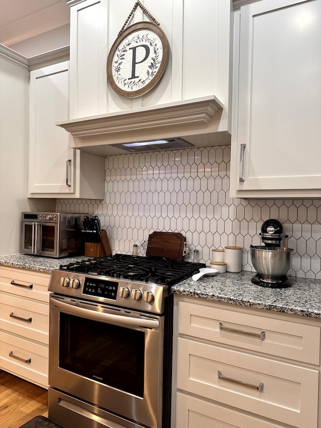 kitchen with light stone countertops, wood-type flooring, stainless steel gas stove, decorative backsplash, and custom range hood