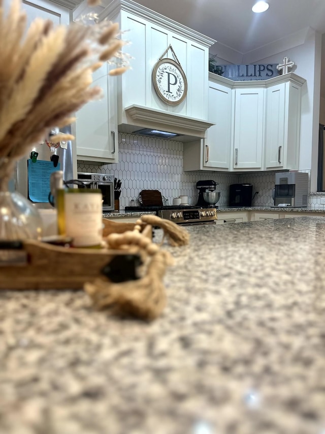 kitchen featuring backsplash, white cabinetry, light stone countertops, and custom range hood