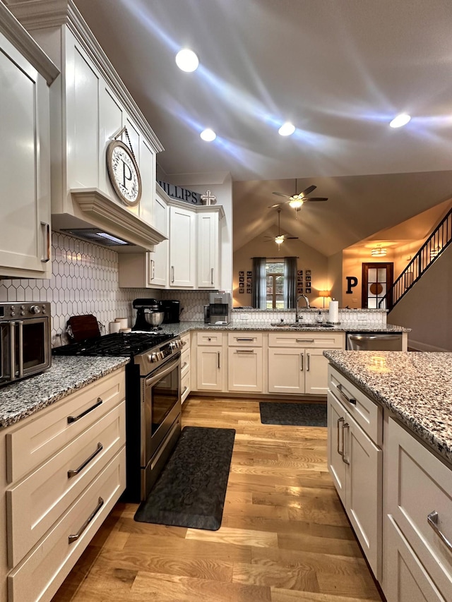 kitchen featuring kitchen peninsula, appliances with stainless steel finishes, sink, backsplash, and light stone countertops