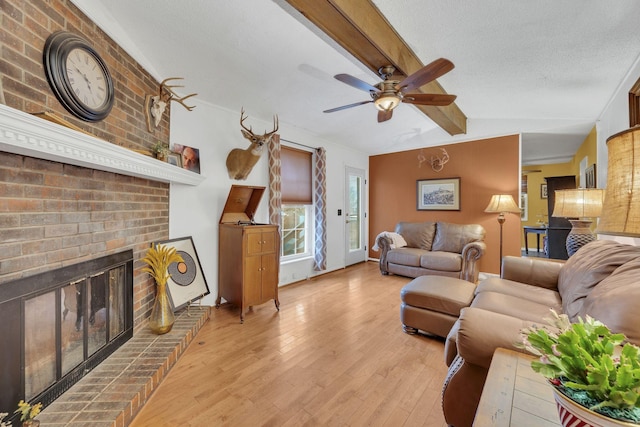 living room with a textured ceiling, vaulted ceiling, a fireplace, light wood-type flooring, and ceiling fan