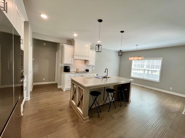 kitchen featuring pendant lighting, sink, white cabinets, tasteful backsplash, and a kitchen island with sink