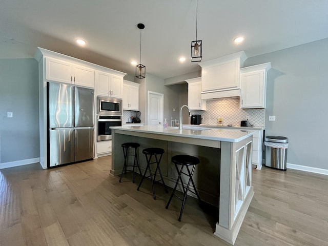 kitchen featuring appliances with stainless steel finishes, white cabinetry, a kitchen island with sink, pendant lighting, and a breakfast bar