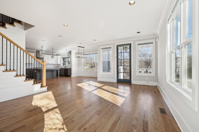 unfurnished living room featuring dark wood-style flooring, recessed lighting, visible vents, ornamental molding, and stairs