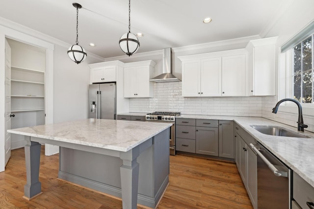 kitchen featuring ornamental molding, gray cabinets, stainless steel appliances, wall chimney range hood, and a sink