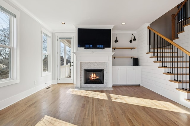 unfurnished living room with baseboards, a fireplace with flush hearth, stairway, ornamental molding, and wood finished floors