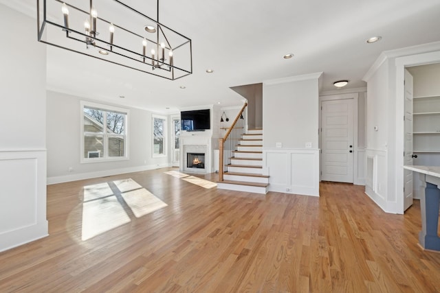 unfurnished living room with a fireplace with flush hearth, light wood-style flooring, ornamental molding, a decorative wall, and recessed lighting