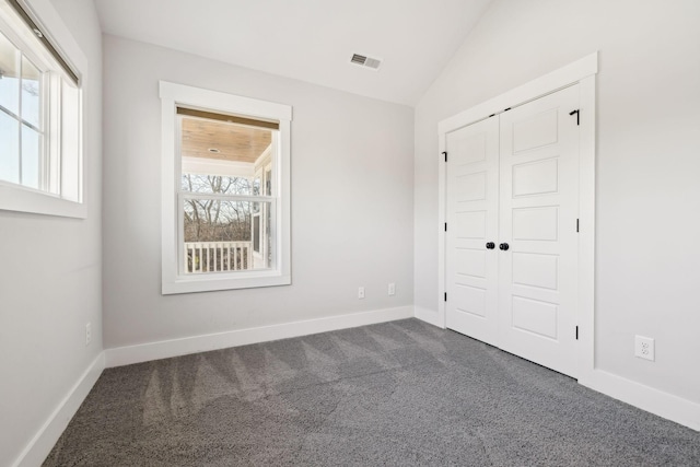 unfurnished bedroom featuring visible vents, multiple windows, dark carpet, and vaulted ceiling