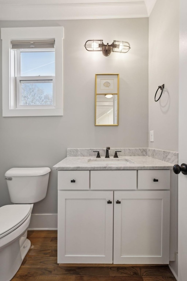 bathroom featuring toilet, wood finished floors, vanity, baseboards, and crown molding