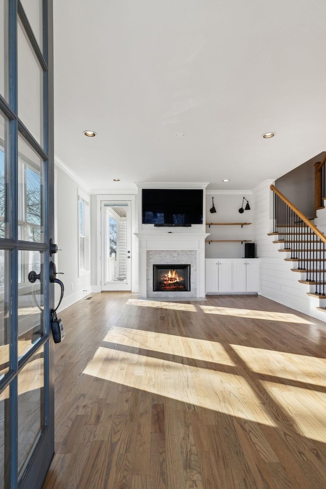 unfurnished living room with a fireplace with flush hearth, ornamental molding, wood finished floors, stairs, and recessed lighting