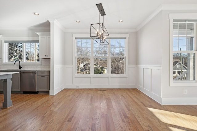 unfurnished dining area featuring light wood finished floors, an inviting chandelier, a sink, and crown molding