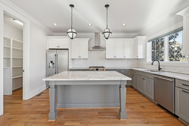 kitchen featuring appliances with stainless steel finishes, ornamental molding, gray cabinets, wall chimney range hood, and a sink