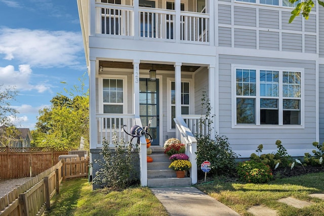 entrance to property with a porch, fence, and a balcony