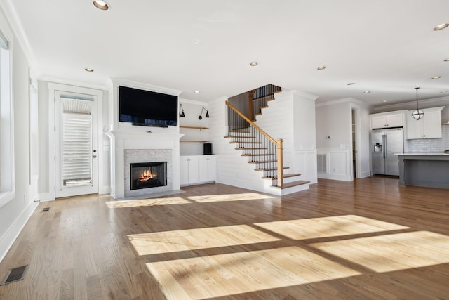 unfurnished living room with wood finished floors, visible vents, crown molding, and stairs