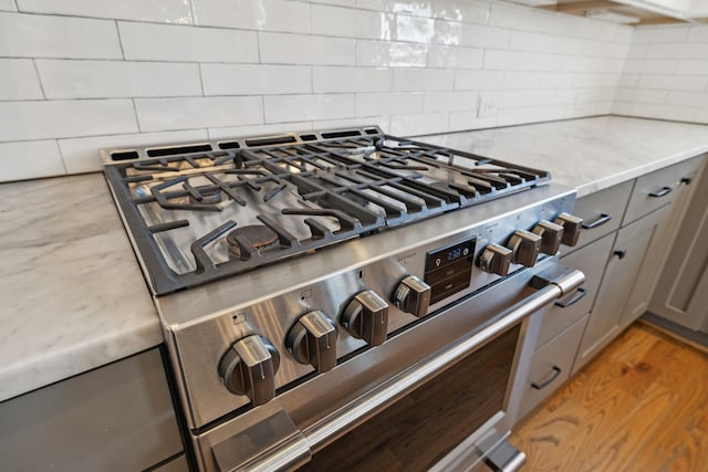 details with tasteful backsplash, high end range, wood finished floors, light stone countertops, and gray cabinets