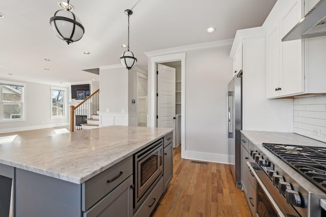 kitchen with under cabinet range hood, gray cabinetry, stainless steel appliances, light wood finished floors, and tasteful backsplash