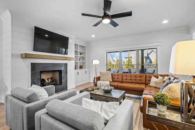 living room with crown molding, ceiling fan, light wood-type flooring, built in shelves, and a fireplace