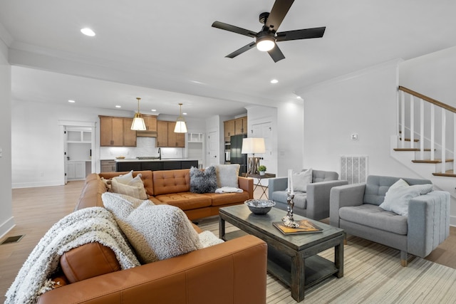 living room featuring ceiling fan, ornamental molding, and light wood-type flooring