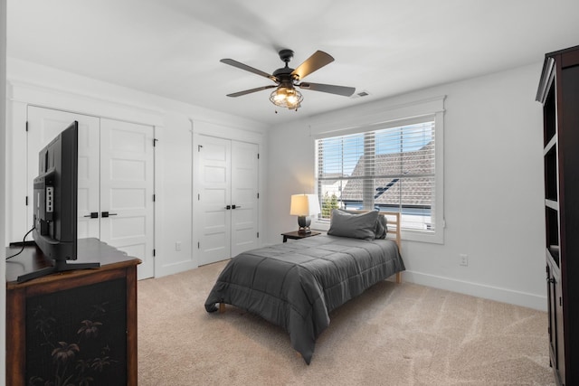 bedroom featuring ceiling fan, light colored carpet, and two closets