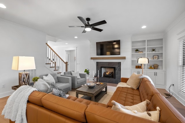 living room with crown molding, ceiling fan, light wood-type flooring, built in shelves, and a tile fireplace