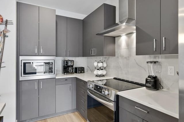 kitchen featuring wall chimney range hood, stainless steel appliances, decorative backsplash, light hardwood / wood-style floors, and gray cabinetry