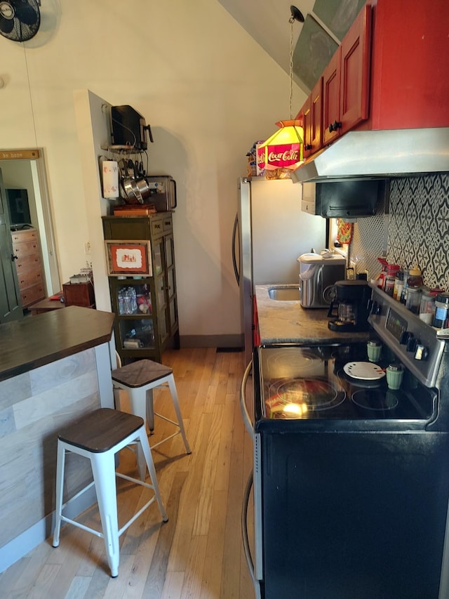 kitchen with range with electric cooktop, stainless steel refrigerator, decorative backsplash, light hardwood / wood-style flooring, and vaulted ceiling