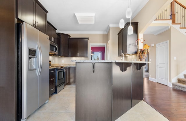 kitchen with appliances with stainless steel finishes, hanging light fixtures, dark brown cabinets, ornamental molding, and a breakfast bar