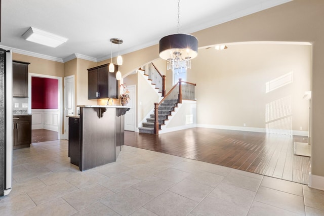 kitchen with a kitchen bar, hanging light fixtures, dark brown cabinets, ornamental molding, and light tile patterned flooring