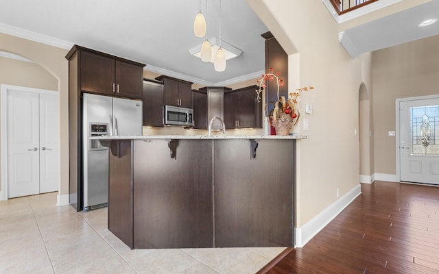 kitchen with crown molding, decorative light fixtures, kitchen peninsula, a breakfast bar, and stainless steel appliances