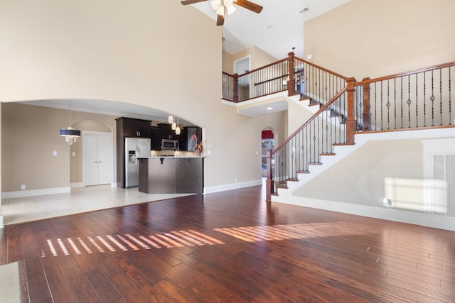 unfurnished living room with a towering ceiling, ceiling fan with notable chandelier, and dark hardwood / wood-style floors