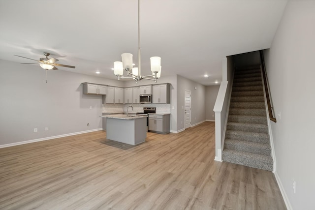 kitchen featuring gray cabinets, backsplash, open floor plan, appliances with stainless steel finishes, and light wood finished floors