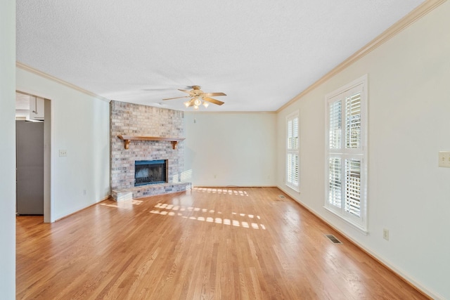 unfurnished living room with crown molding, light wood-type flooring, a textured ceiling, and a brick fireplace