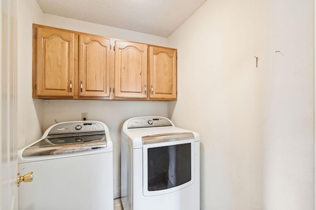 washroom with cabinets, a textured ceiling, and washing machine and clothes dryer