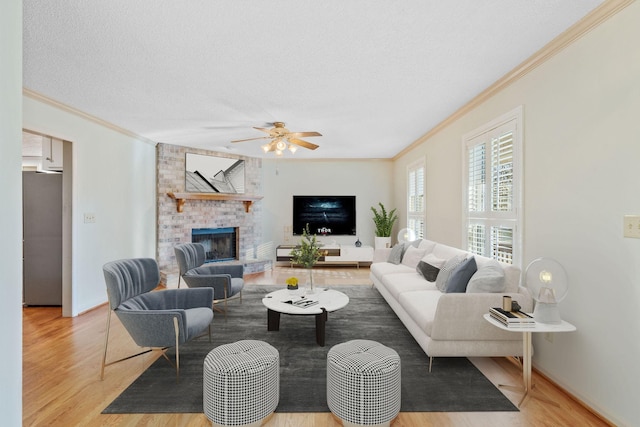 living room featuring ceiling fan, a brick fireplace, a textured ceiling, ornamental molding, and light hardwood / wood-style floors