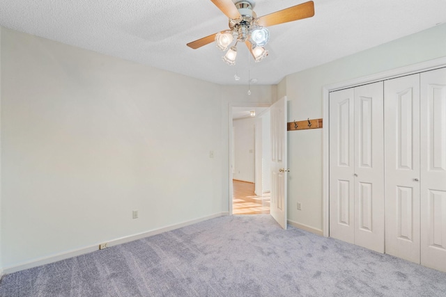 unfurnished bedroom with a closet, ceiling fan, light colored carpet, and a textured ceiling