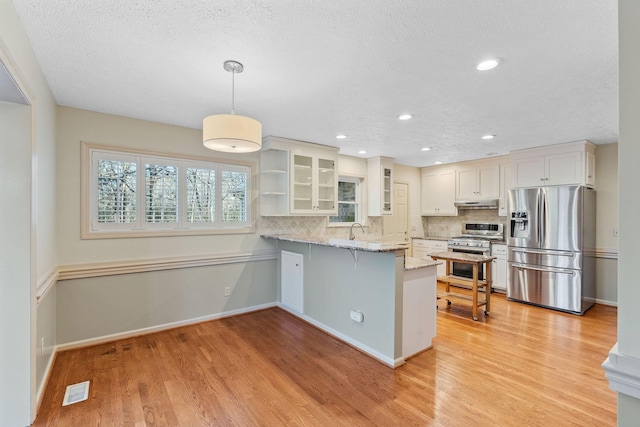 kitchen with appliances with stainless steel finishes, white cabinetry, decorative backsplash, hanging light fixtures, and kitchen peninsula