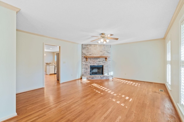 unfurnished living room featuring light wood-type flooring, a wealth of natural light, a brick fireplace, and ornamental molding