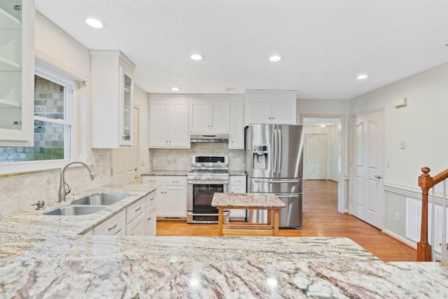 kitchen with sink, white cabinets, light wood-type flooring, stainless steel appliances, and light stone counters