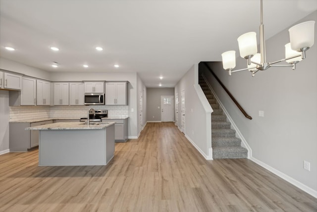 kitchen featuring pendant lighting, appliances with stainless steel finishes, light wood-type flooring, gray cabinetry, and light stone counters