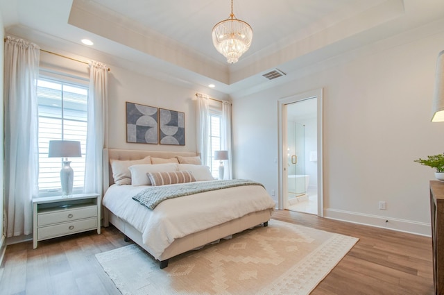 bedroom with hardwood / wood-style floors, a tray ceiling, ensuite bathroom, and a chandelier