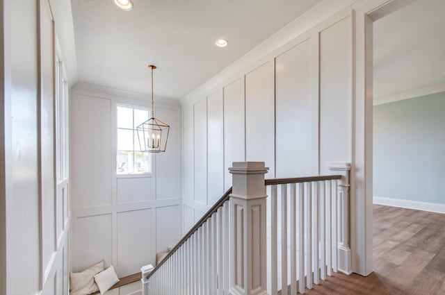 stairway featuring wood-type flooring, ornamental molding, and an inviting chandelier