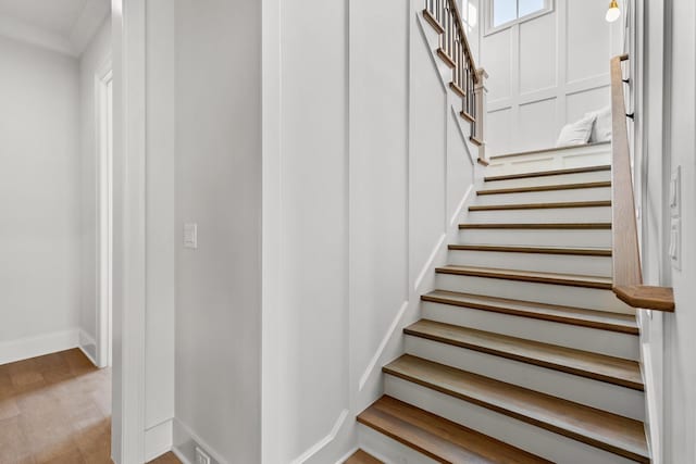 stairs featuring wood-type flooring and crown molding