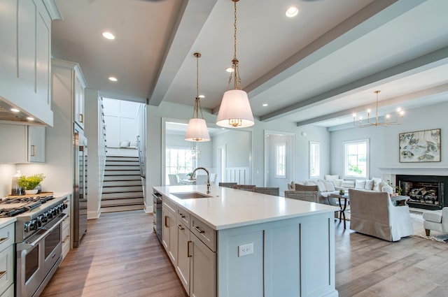 kitchen with hanging light fixtures, sink, a kitchen island with sink, beamed ceiling, and stainless steel appliances