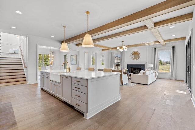 kitchen featuring decorative light fixtures, sink, light wood-type flooring, a kitchen island with sink, and beamed ceiling