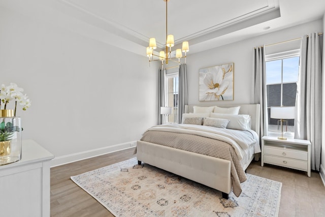 bedroom with light hardwood / wood-style floors, a tray ceiling, and a chandelier