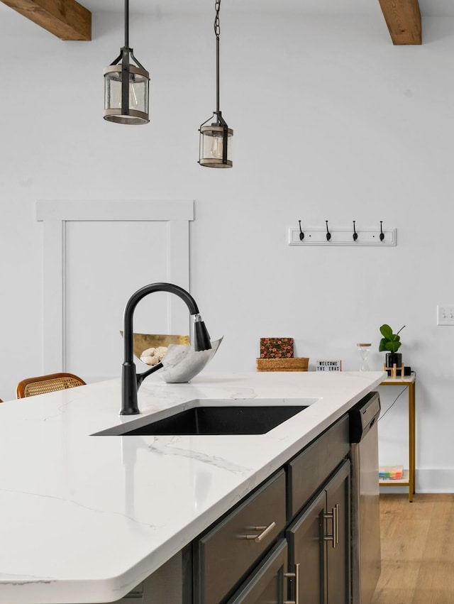 interior space featuring light stone countertops, hanging light fixtures, stainless steel dishwasher, sink, and light hardwood / wood-style flooring